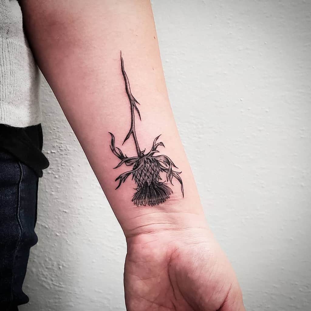A forearm tattoo showcasing an exquisitely detailed black thistle elegantly etched into the skin