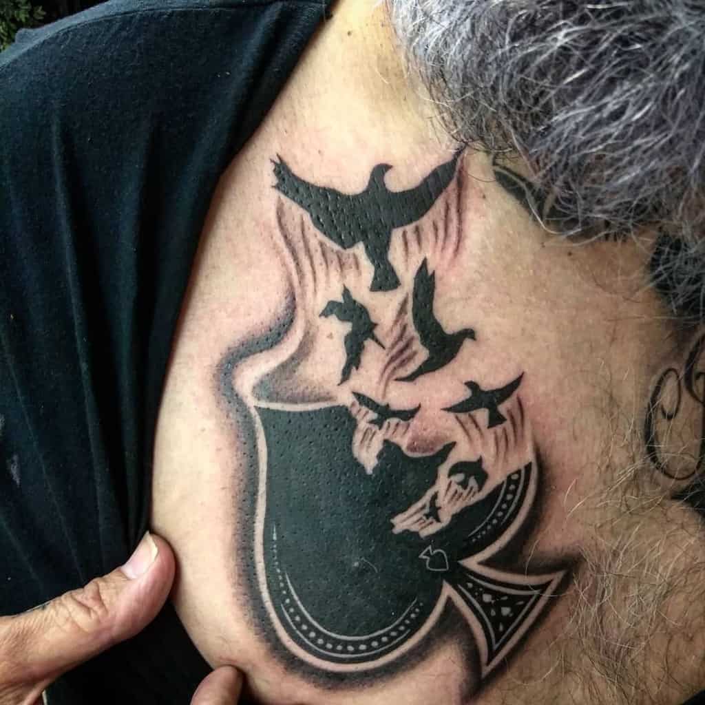 A black-and-white tattoo of the Ace of Spades, with birds flying out of it