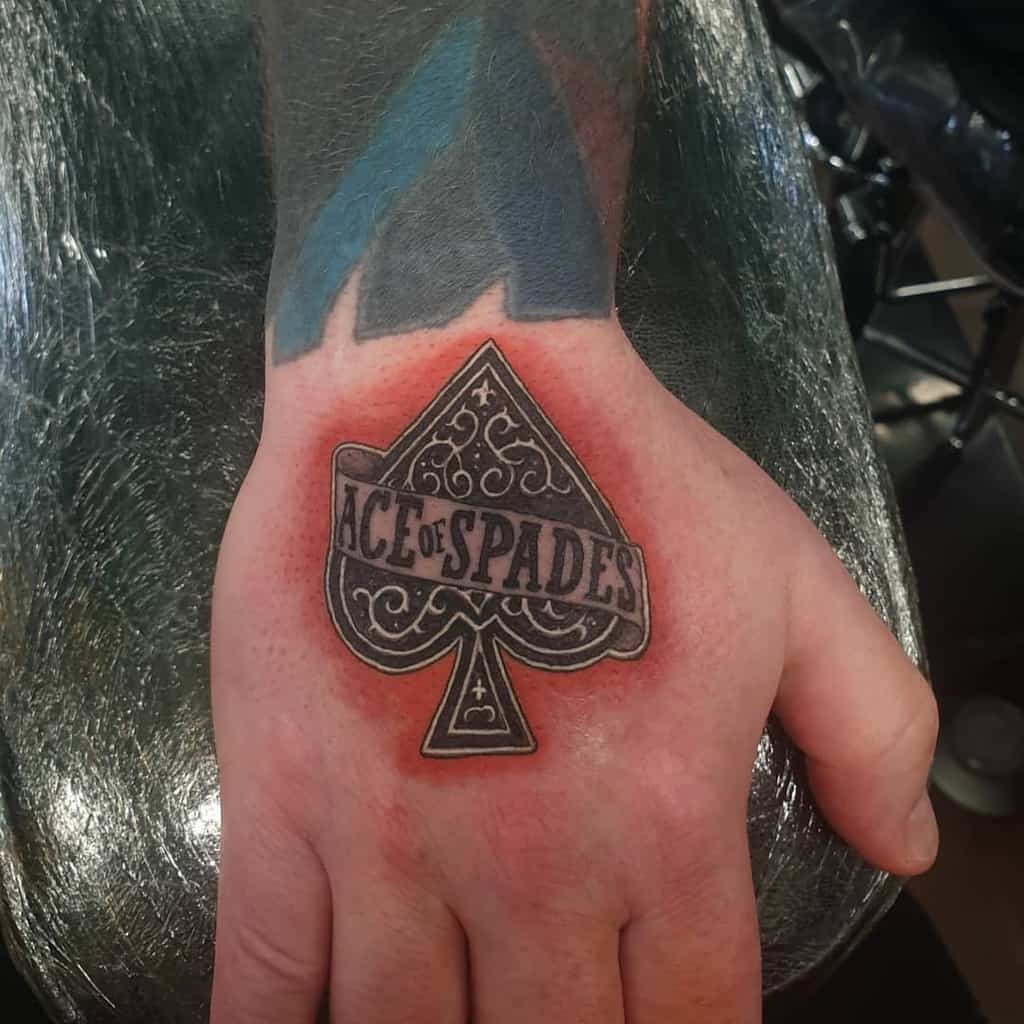 A black-and-white tattoo of the spade design with ornate details and the words "Ace of Spades" written across it, set against a shaded red background