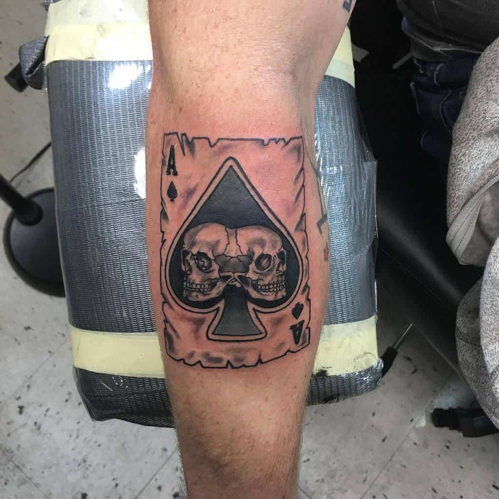 A black-and-white tattoo of the Ace of Spades card with two skulls in the center