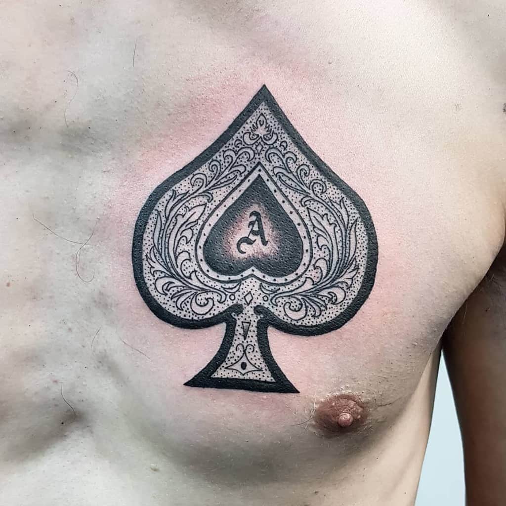 A black-and-white tattoo of the Ace of Spades symbol, featuring intricate detailing and shading