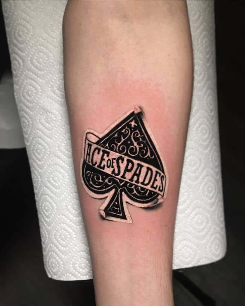 A black-and-white tattoo of the Ace of Spades symbol with intricate detailing, with the words "ACE OF SPADES"