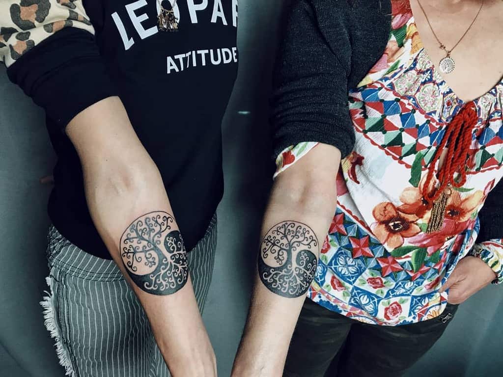 Matching forearm tattoos featuring a circular tree of life design with intricate blackwork patterns, symbolizing connection