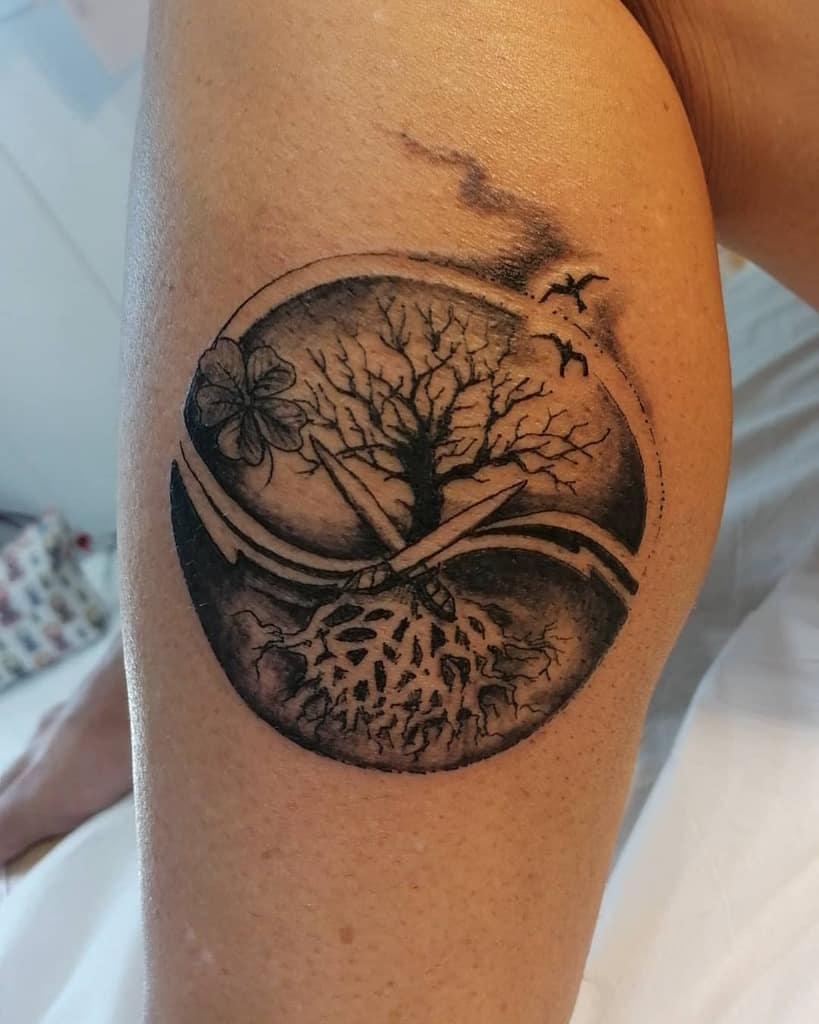 Black and grey tattoo of a circular tree of life with roots, floral accents, flying birds, and abstract flowing elements