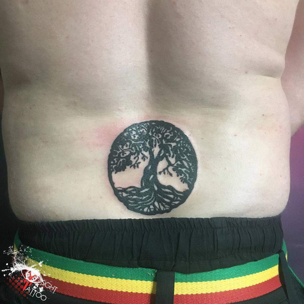 Lower back tattoo featuring a bold blackwork tree of life design enclosed in a circular silhouette, symbolizing unity