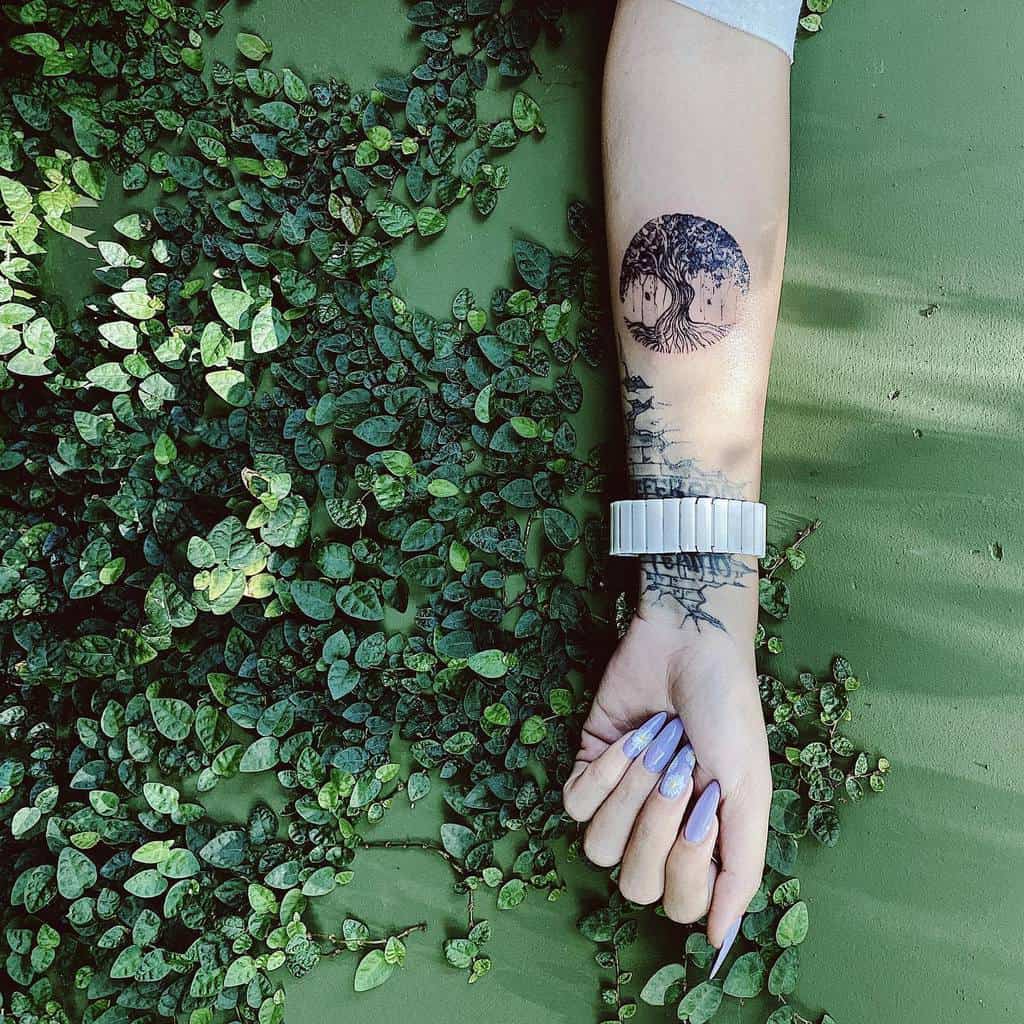 Delicate forearm tattoo of a circular tree of life design, blending detailed roots and branches with nature-inspired surroundings