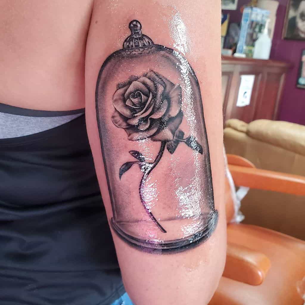 A realistic black and grey Beauty and the Beast rose tattoo inside a glass dome, featuring detailed shading and fine lines
