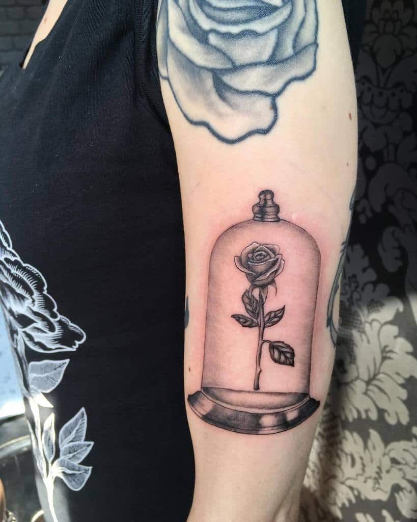 A clean black and grey tattoo of the Beauty and the Beast rose inside a glass dome, featuring fine details and shading