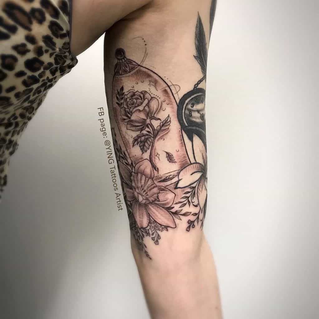 A beautiful black and grey tattoo of the Beauty and the Beast rose inside a glass dome, surrounded by additional flowers and delicate detailing