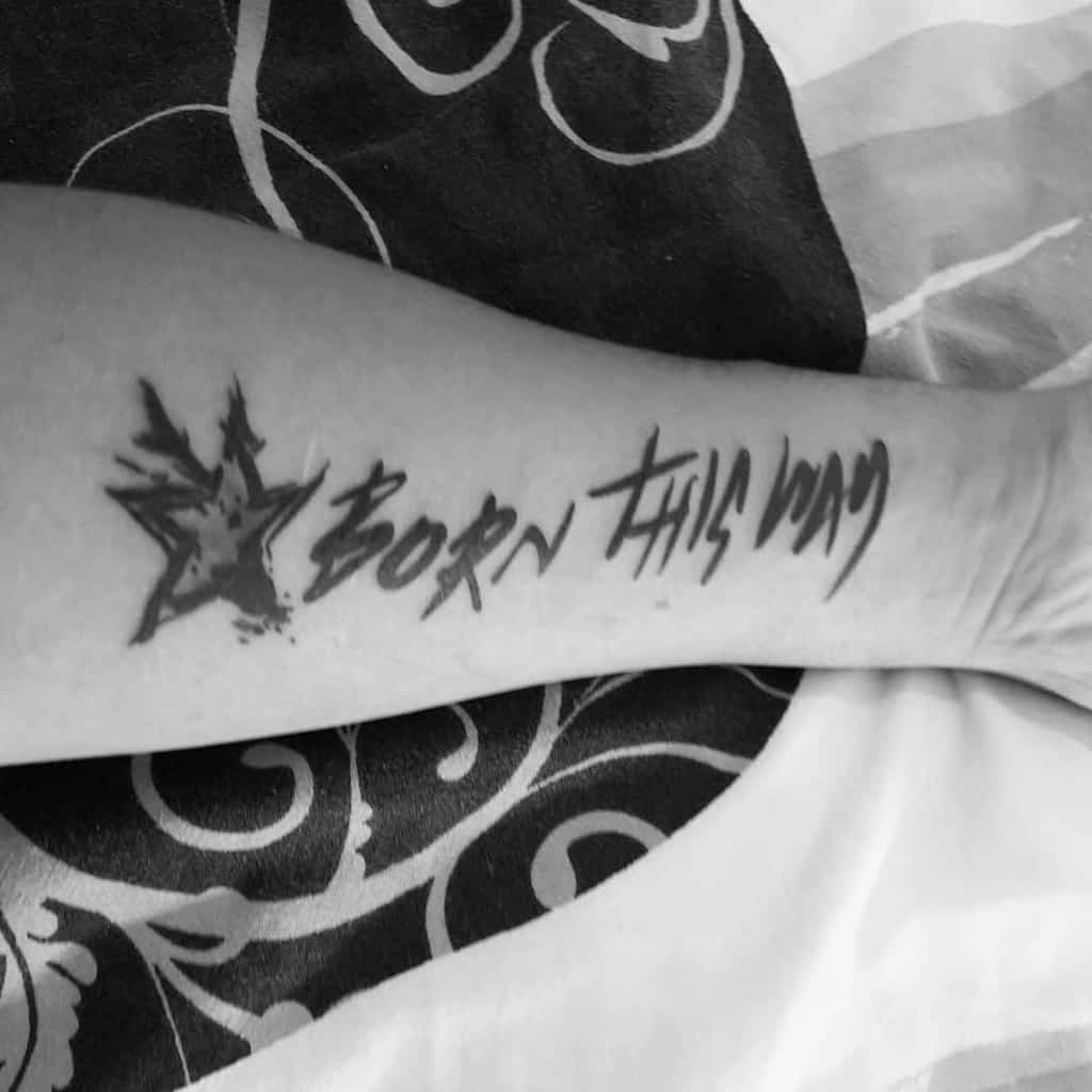 Black and white tattoo on an arm reading "BORN THIS WAY" with a star design