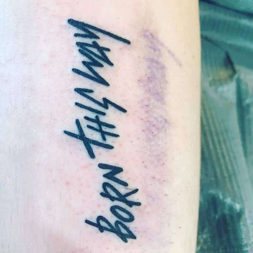 Tattoo on arm reading "Born This Way" in bold script font