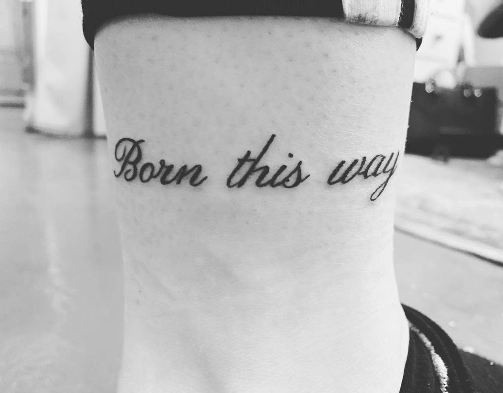 A black and white tattoo on an ankle that reads "Born this way"