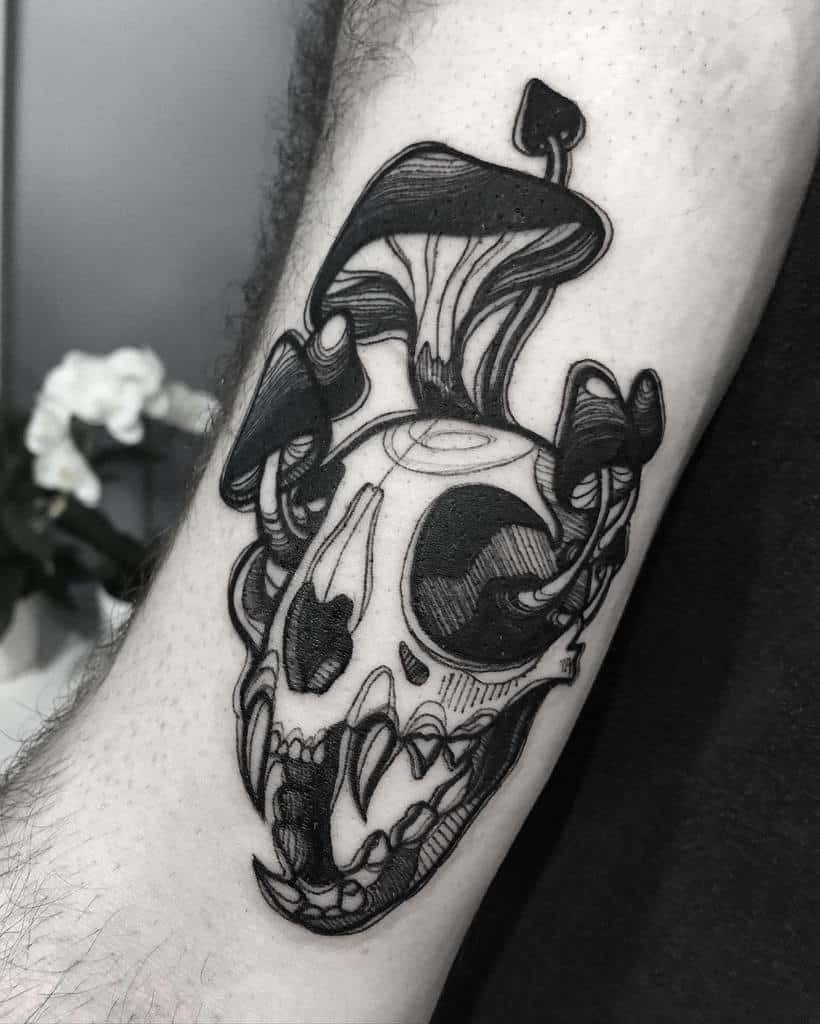 Black and white tattoo of a cat skull with mushrooms growing out of it on an arm