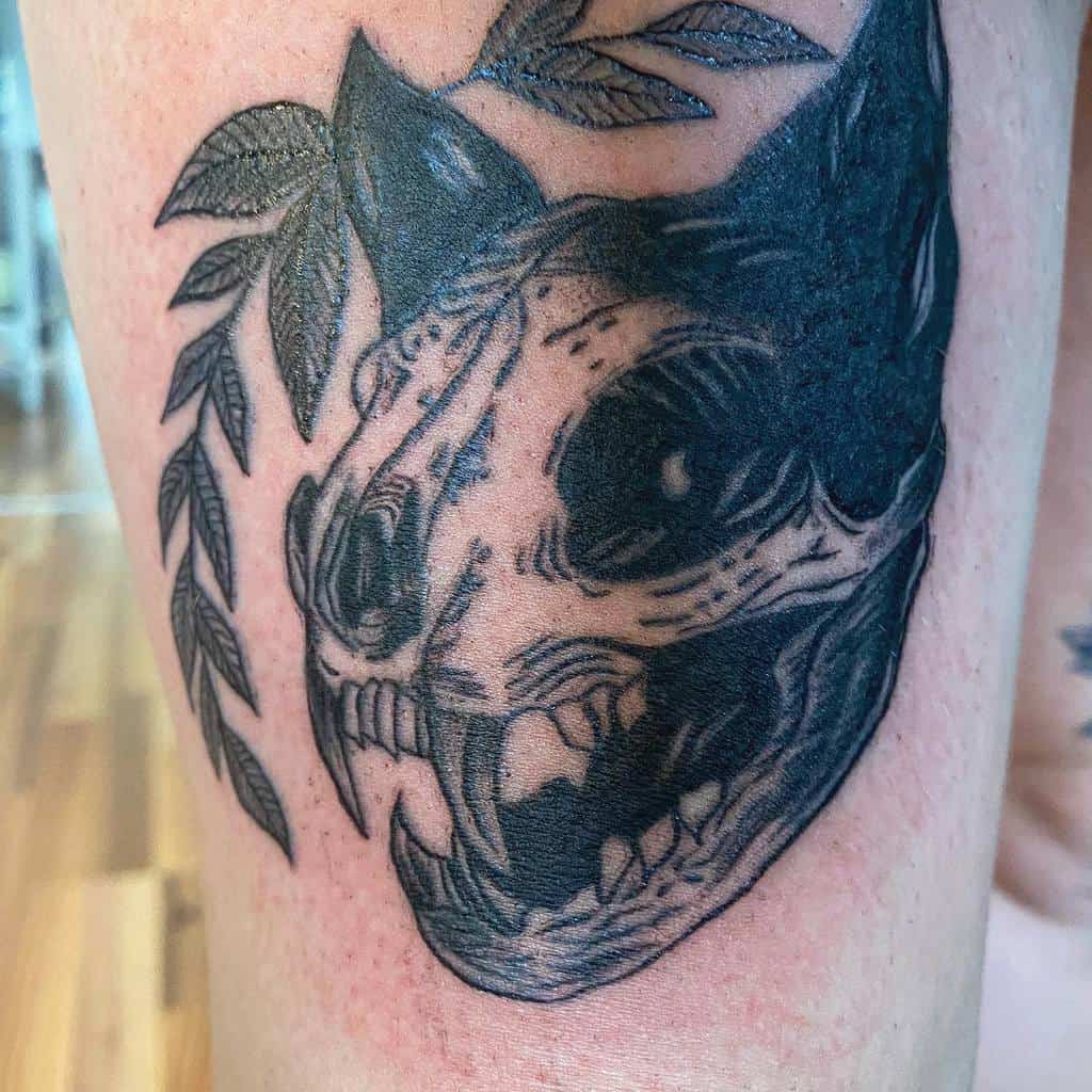Tattoo of a cat skull entwined with leaves on a leg