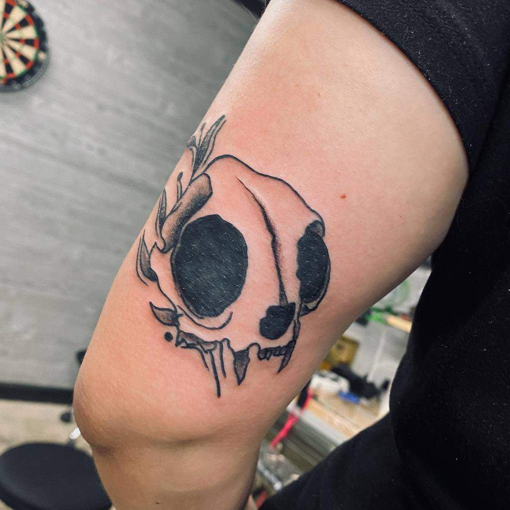 Tattoo of a cat skull with large eye sockets on the upper arm