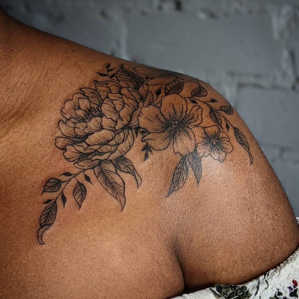 A beautiful floral tattoo graces a person's shoulder, showcasing detailed peonies and leaves in an exquisite design