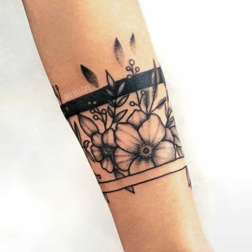 Black ink floral tattoo with dogwood flowers, leaves, and geometric lines, wrapped around the wrist