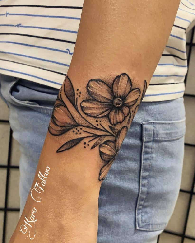 A forearm tattoo of detailed flowers and leaves gracefully flows down to the wrist