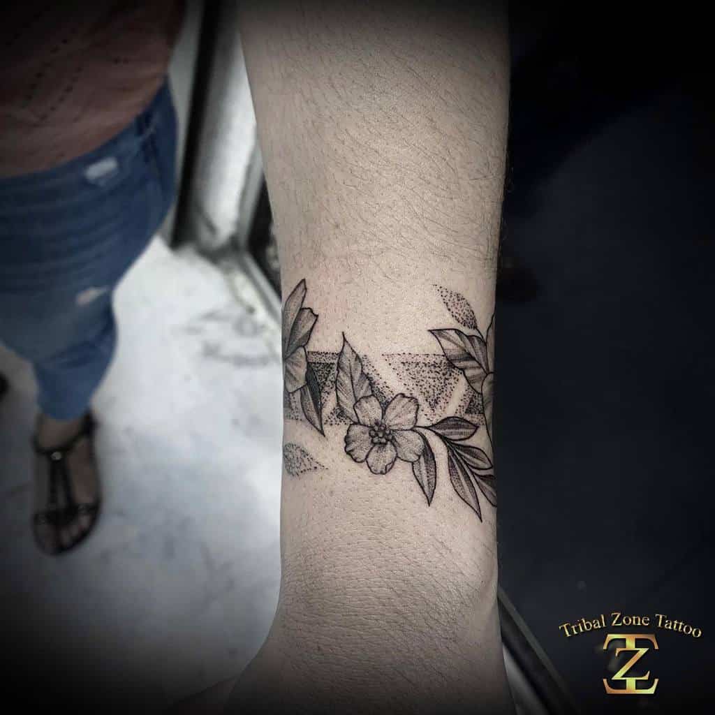 Blackwork floral tattoo featuring dogwood flowers, leaves, and geometric bands, wrapped around the wrist
