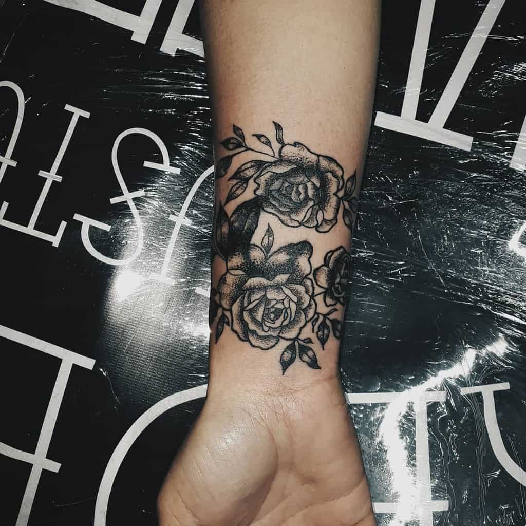 A black ink floral tattoo elegantly wraps around the wrist, featuring detailed roses and leaves