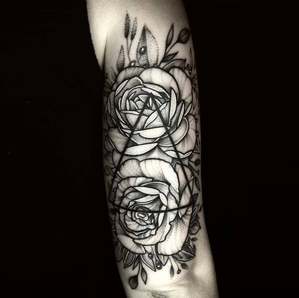 A black and gray tattoo of roses and geometric shapes on an arm