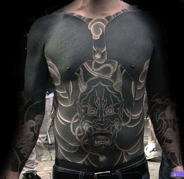 Bold Japanese chest tattoo in blackwork style featuring a menacing demon mask surrounded by intricate patterns and shading