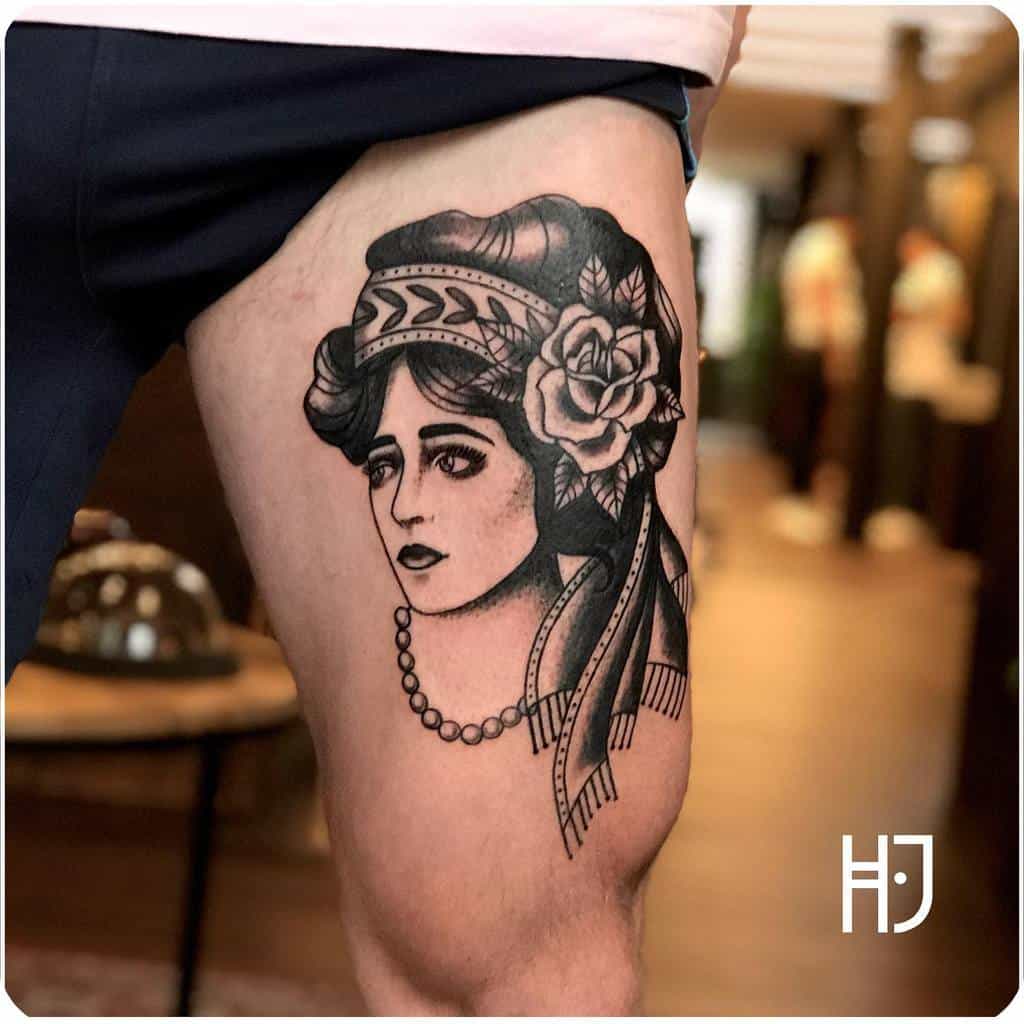 Tattoo of a gypsy woman's face adorned with a flower and headband on a thigh