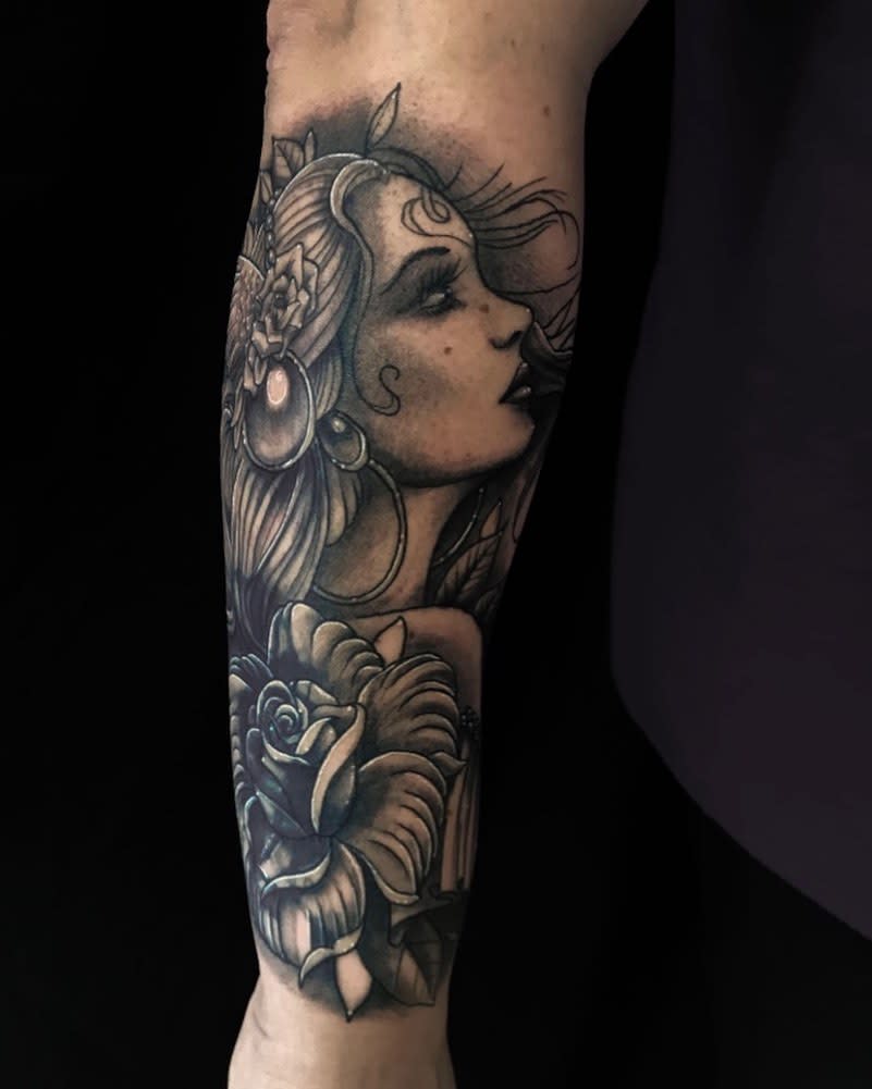 Black and grey tattoo of a gypsy woman with flowers elegantly adorning an arm