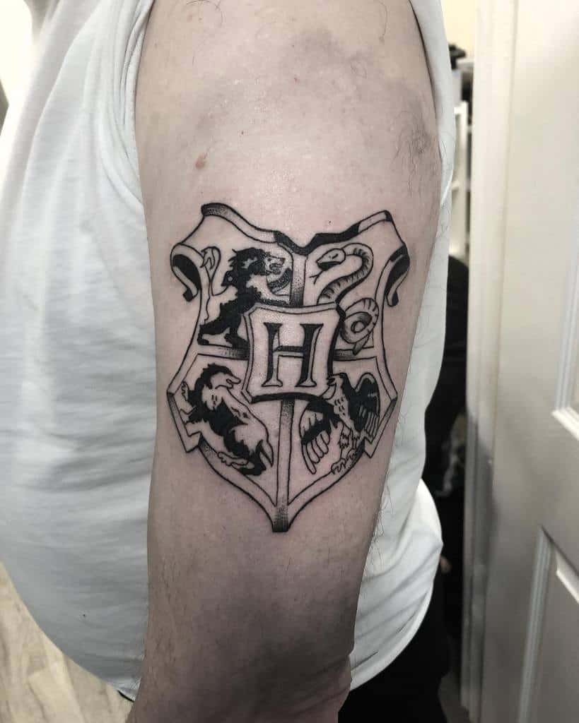 Black and grey Hogwarts crest tattoo, featuring house mascots for Gryffindor, Slytherin, Hufflepuff, and Ravenclaw