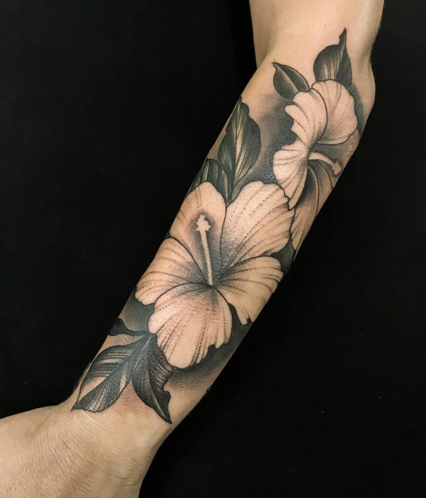 Black and white floral tattoo on forearm, featuring two large hibiscus flowers and leaves