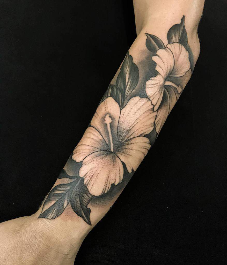 Forearm tattoo featuring large, shaded blooms and leaves on a black background