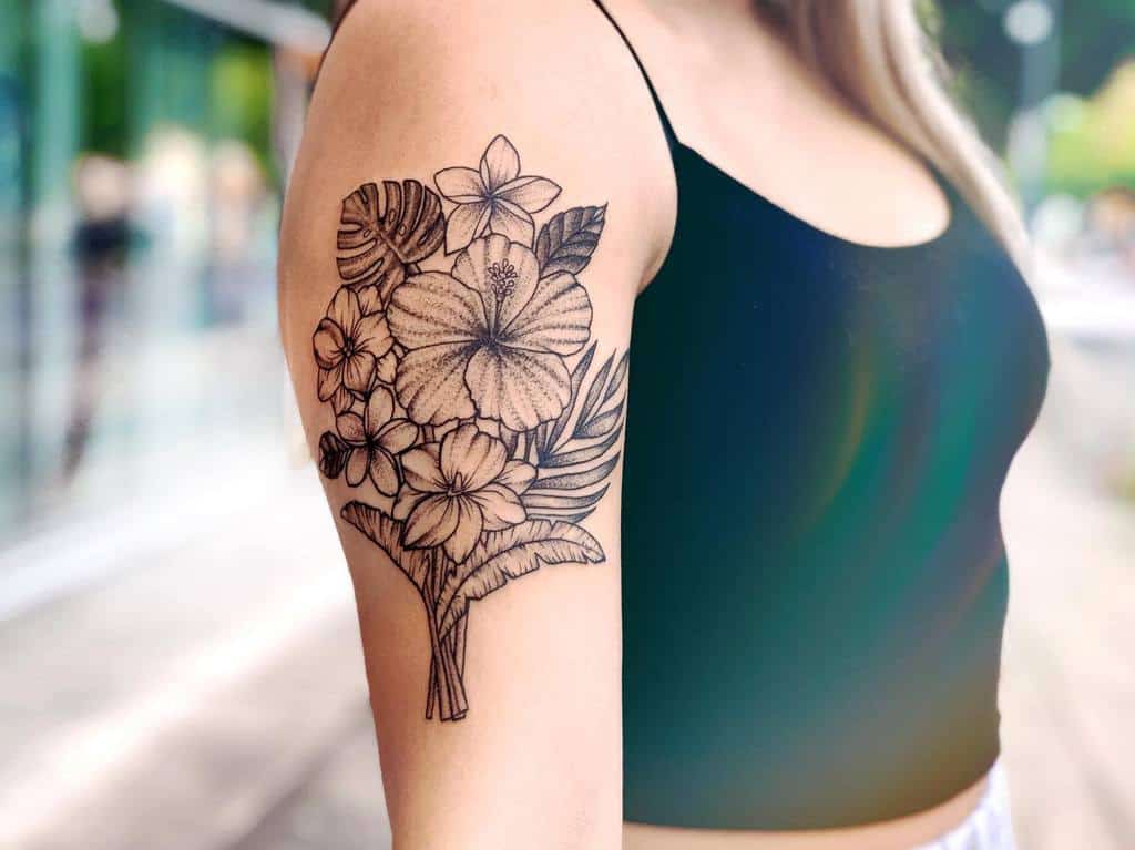 Upper arm tattoo featuring a bouquet of black and grey hibiscus and plumeria flowers with tropical leaves for a detailed floral design