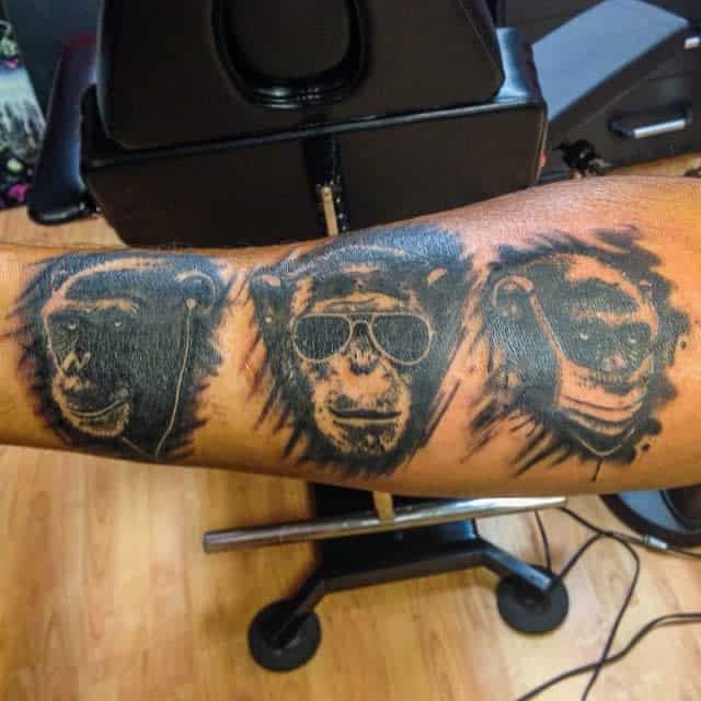 Tattoo of three monkeys on an arm: one with headphones, one with sunglasses, and one with a face mask