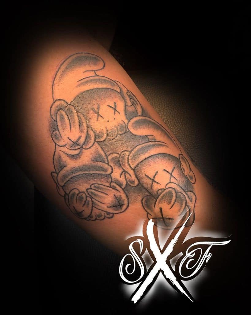 Black and gray tattoo of three cartoonish characters with X-shaped eyes, covering their ears, eyes, and mouth, representing 'Hear No Evil, See No Evil, Speak No Evil'