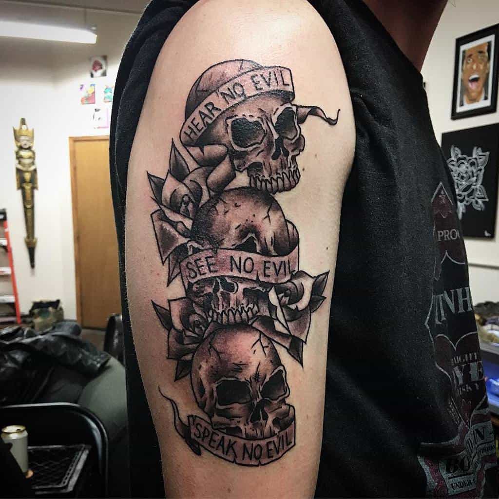 Tattoo of three skulls on an arm with banners reading "Hear No Evil," "See No Evil," "Speak No Evil"