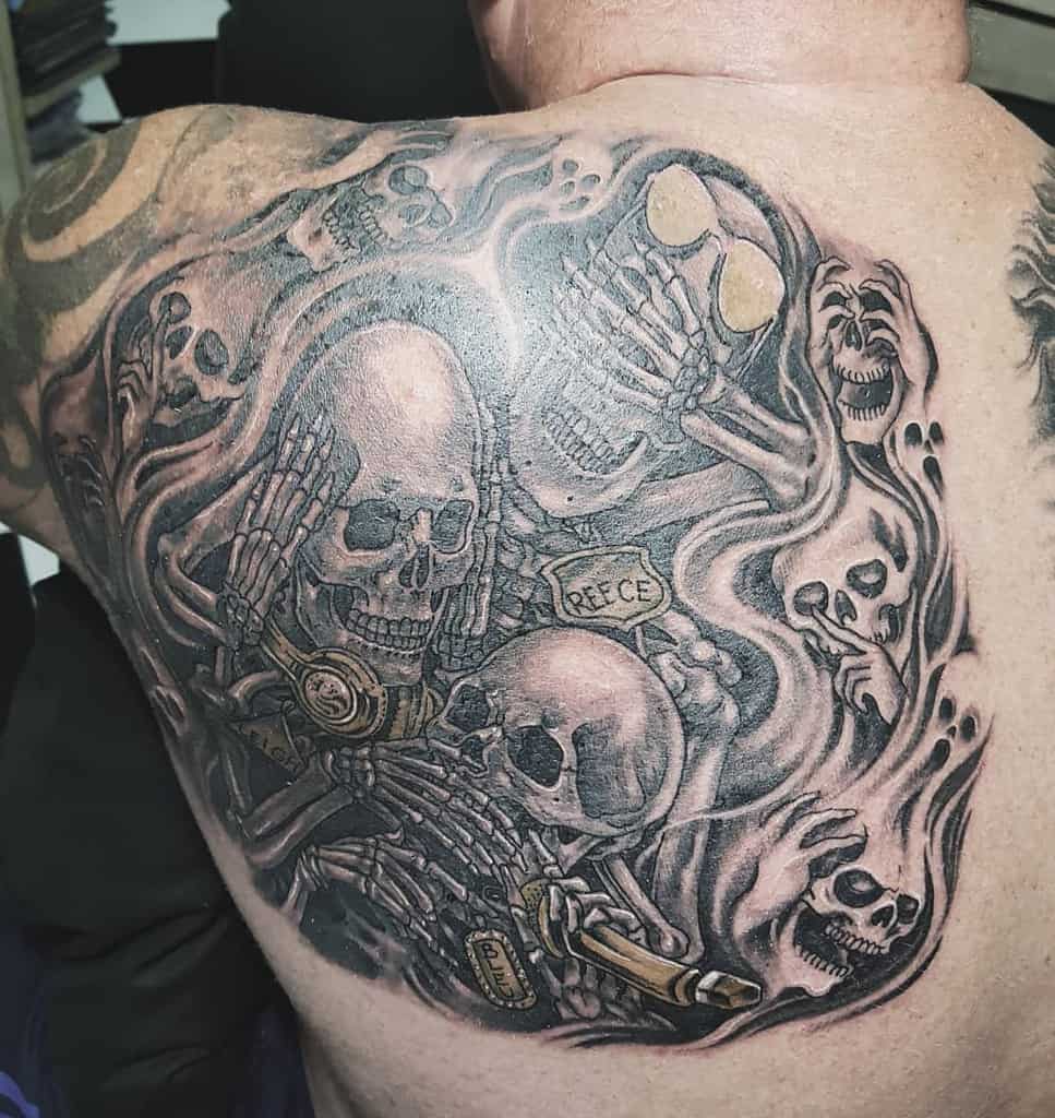 Intricate back tattoo of multiple skulls representing 'Hear No Evil, See No Evil, Speak No Evil,' surrounded by swirling designs and details