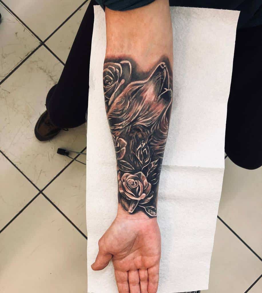 Blackwork tattoo on forearm featuring a detailed howling wolf surrounded by roses, creating a bold and intricate design