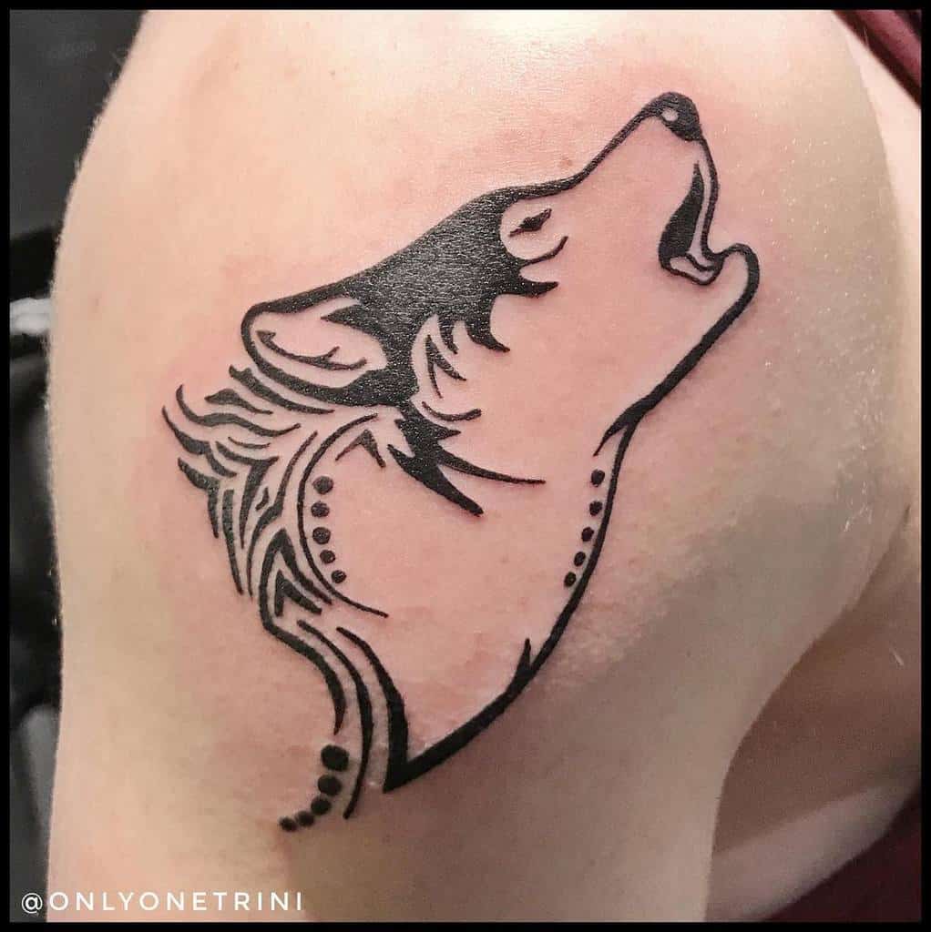 Tattoo of a howling wolf in black ink on a person's skin, the design is stylized and includes decorative lines