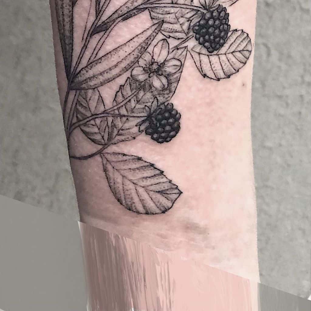 A tattoo of blackberries with leaves and flowers on an arm