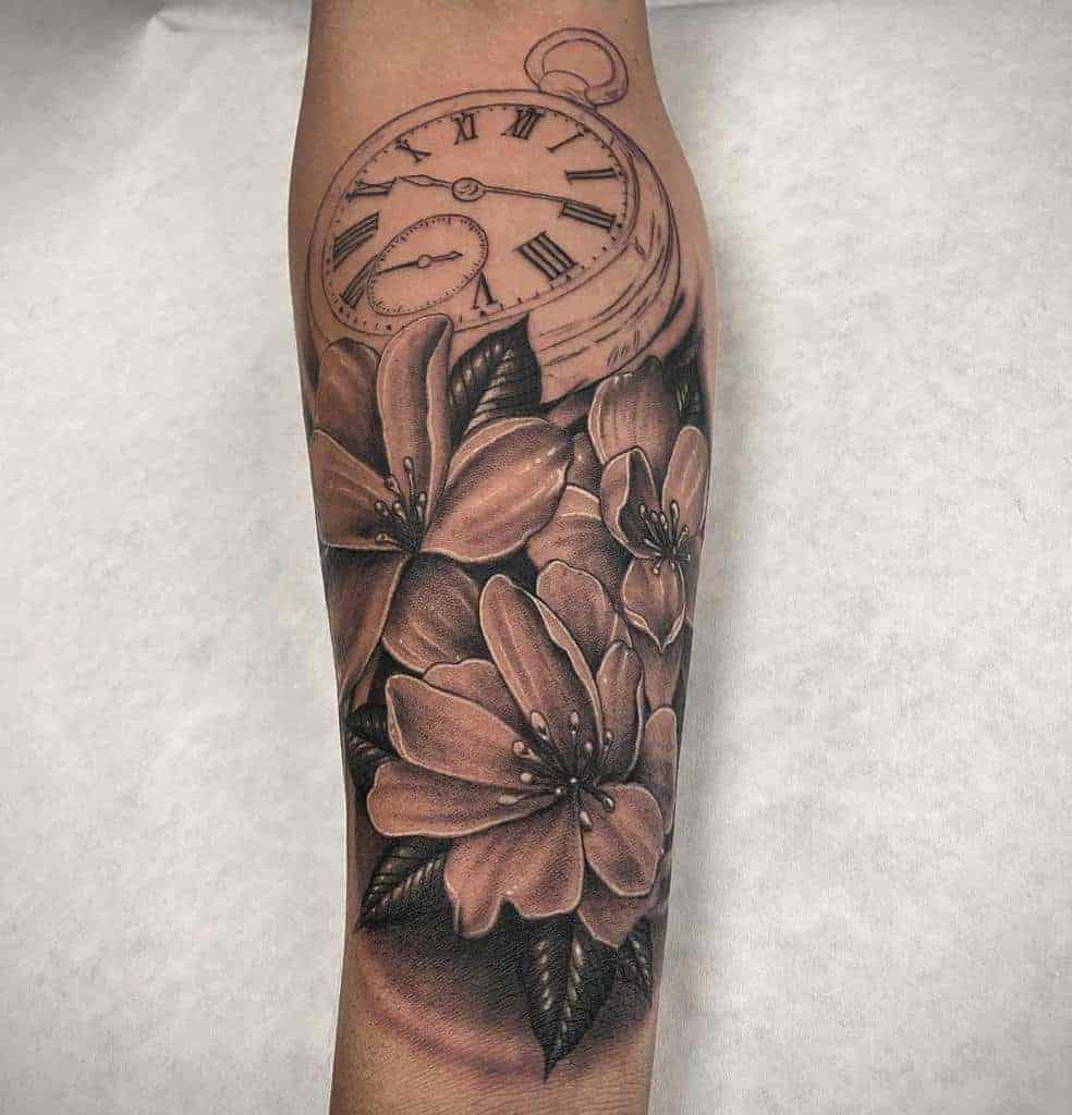 Tattoo of a vintage pocket watch with Roman numerals surrounded by blooming jasmine flowers and leaves on an arm