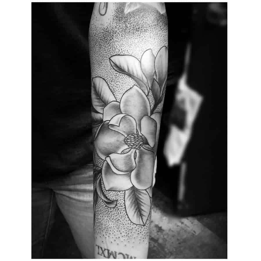 Black and white tattoo of a magnolia flower with leaves elegantly gracing a forearm