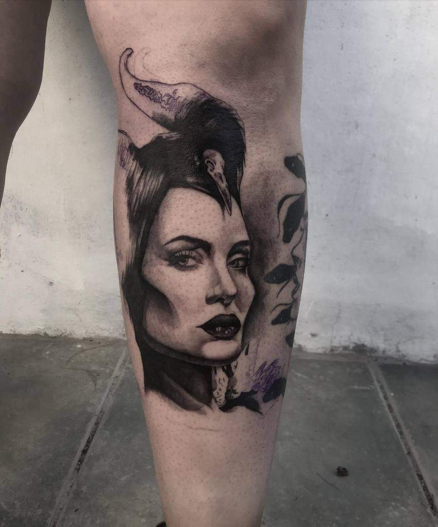 Realistic black-and-grey Maleficent tattoo with detailed shading, iconic horns, and a haunting raven companion on the leg