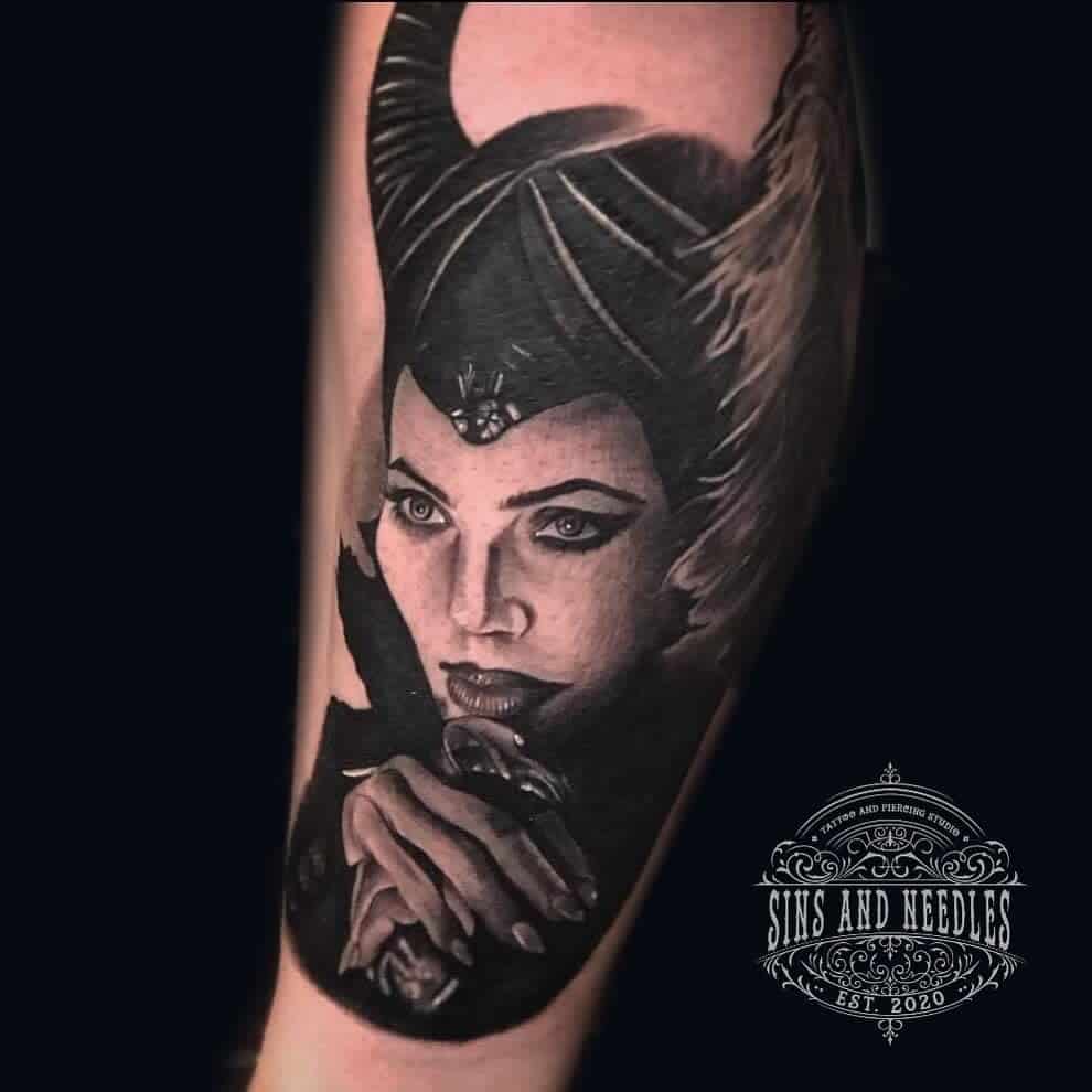 Highly detailed black-and-gray tattoo of Maleficent with a captivating gaze, holding her staff, exuding elegance and power
