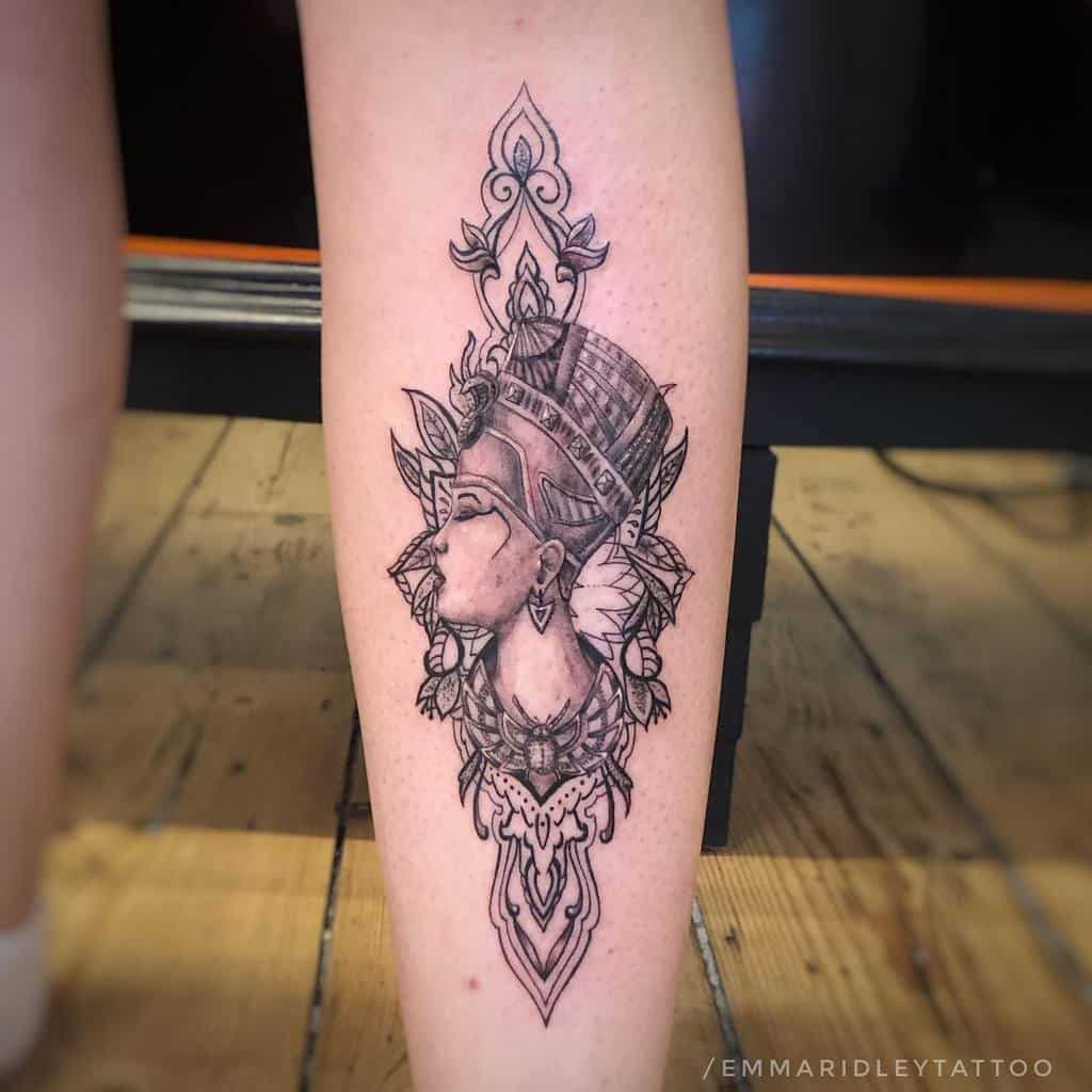 Tattoo of Nefertiti's regal profile with a headdress, in black and grey, on a leg