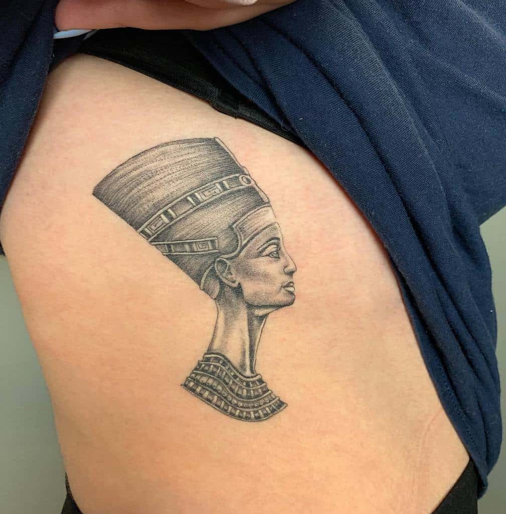 A stunning side-profile tattoo of Queen Nefertiti, showcasing intricate blackwork shading and detailed linework for a regal and timeless design