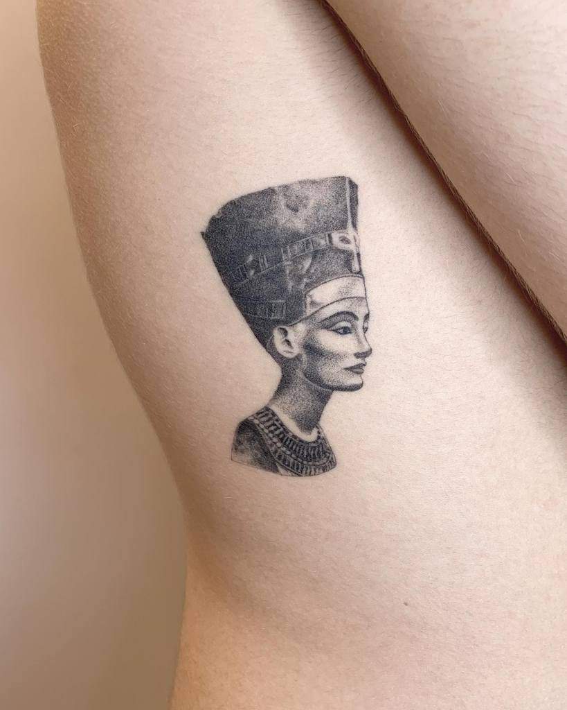 Tattoo of Nefertiti in profile, showcasing her intricate headdress and stunning jewelry
