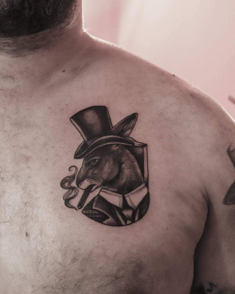 Stylized black and gray tattoo of a rabbit dressed in a suit and top hat, smoking a cigar, with fine detailing and shading