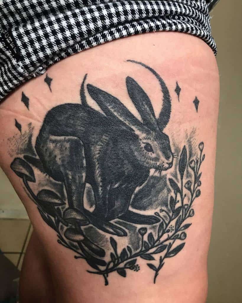 Realistic black and gray tattoo of a rabbit, framed by delicate flowers, leaves, crescent moon and stars