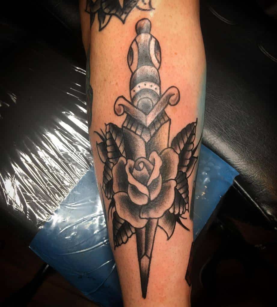 Black tattoo of a dagger piercing a rose on an arm