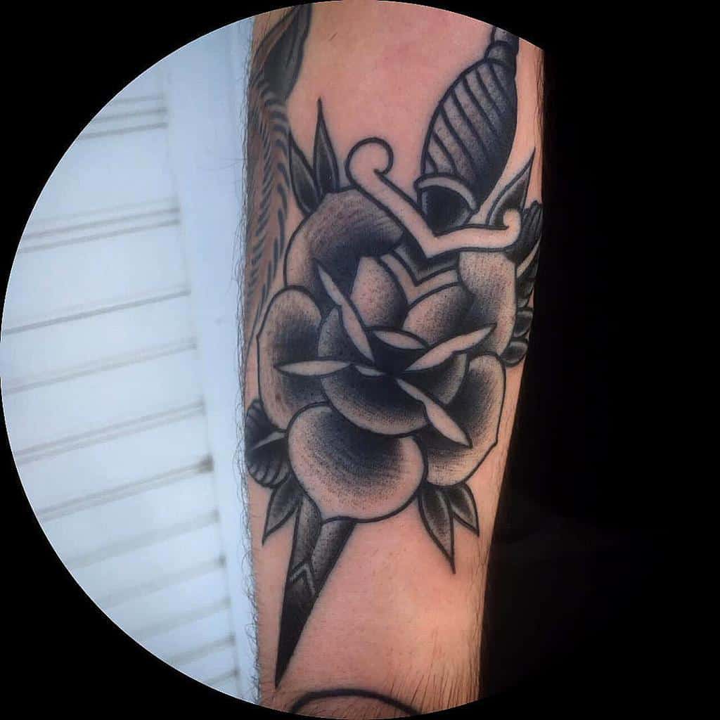 Blackwork rose and dagger tattoo with bold shading and clean lines, creating a classic yet striking design